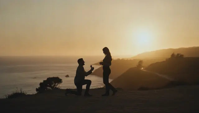 A man kneeling to propose on a hillside at sunset